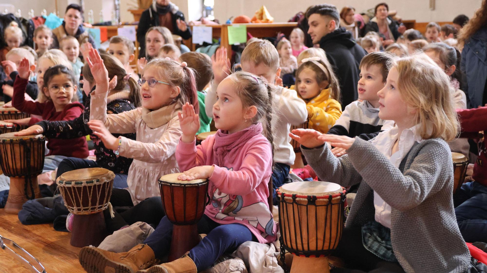 Zahlreiche Kinder sitzen zusammen und trommeln.
