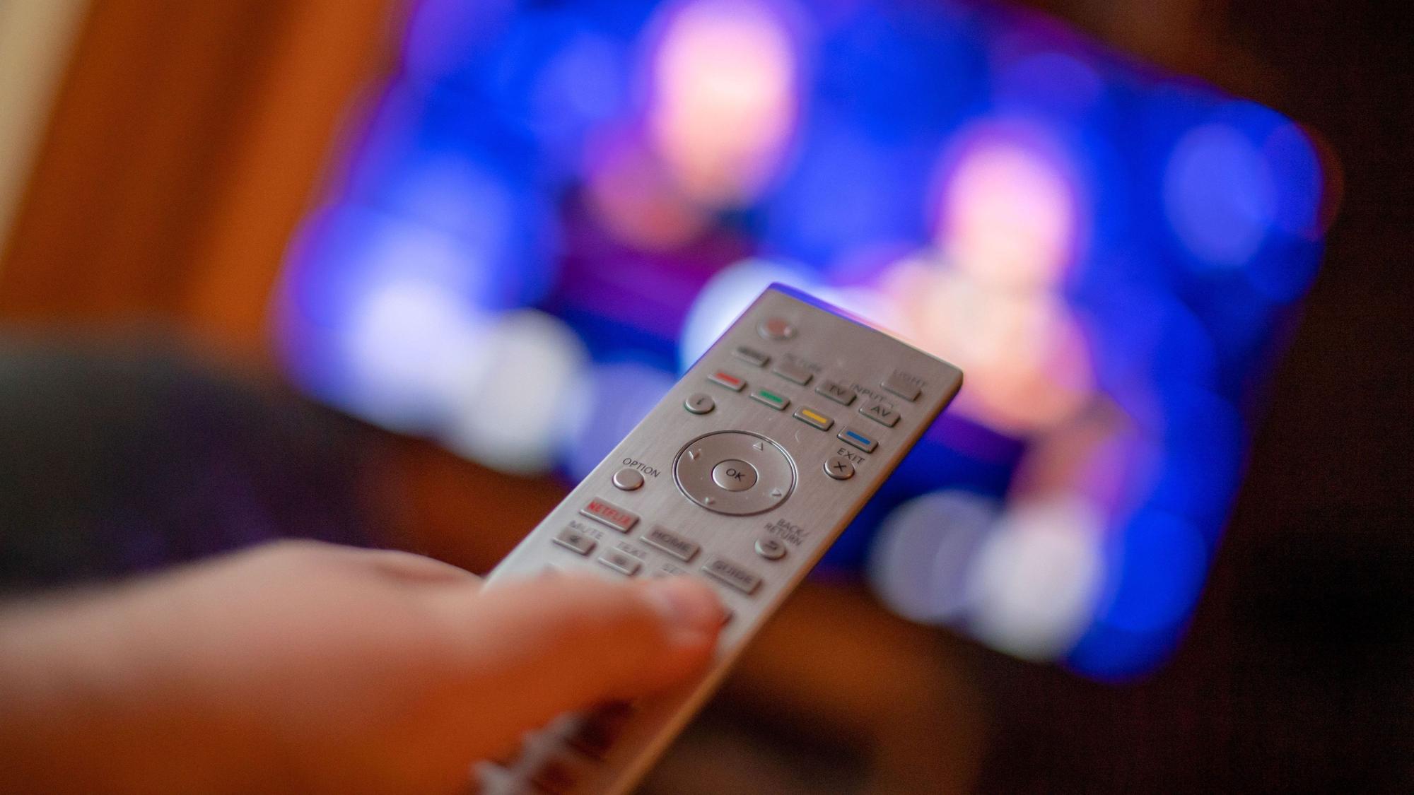 Ein Mann bedient mit der Fernbedienung einen Fernseher (Symbolbild)