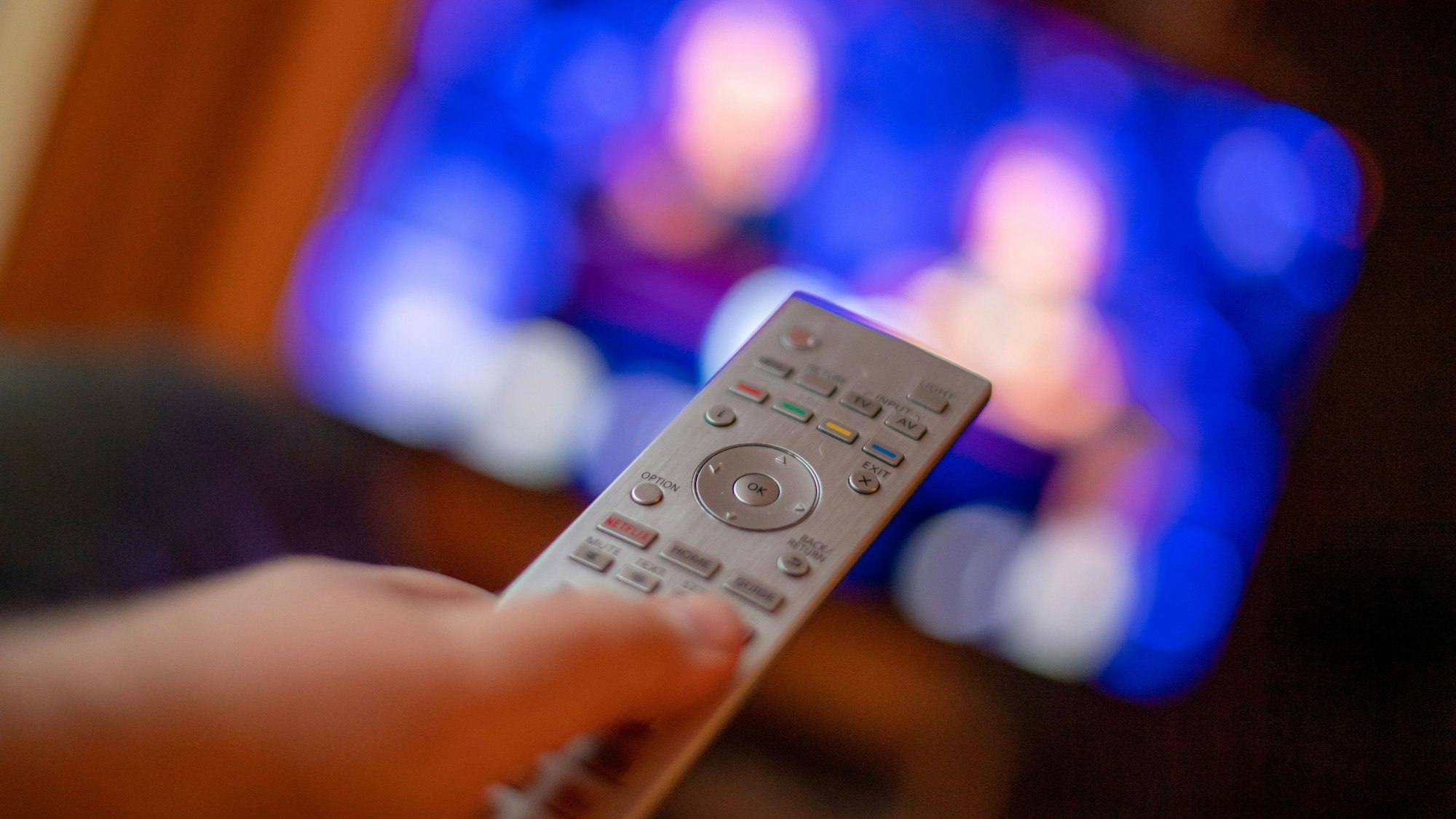 Ein Mann bedient mit der Fernbedienung einen Fernseher (Symbolbild)