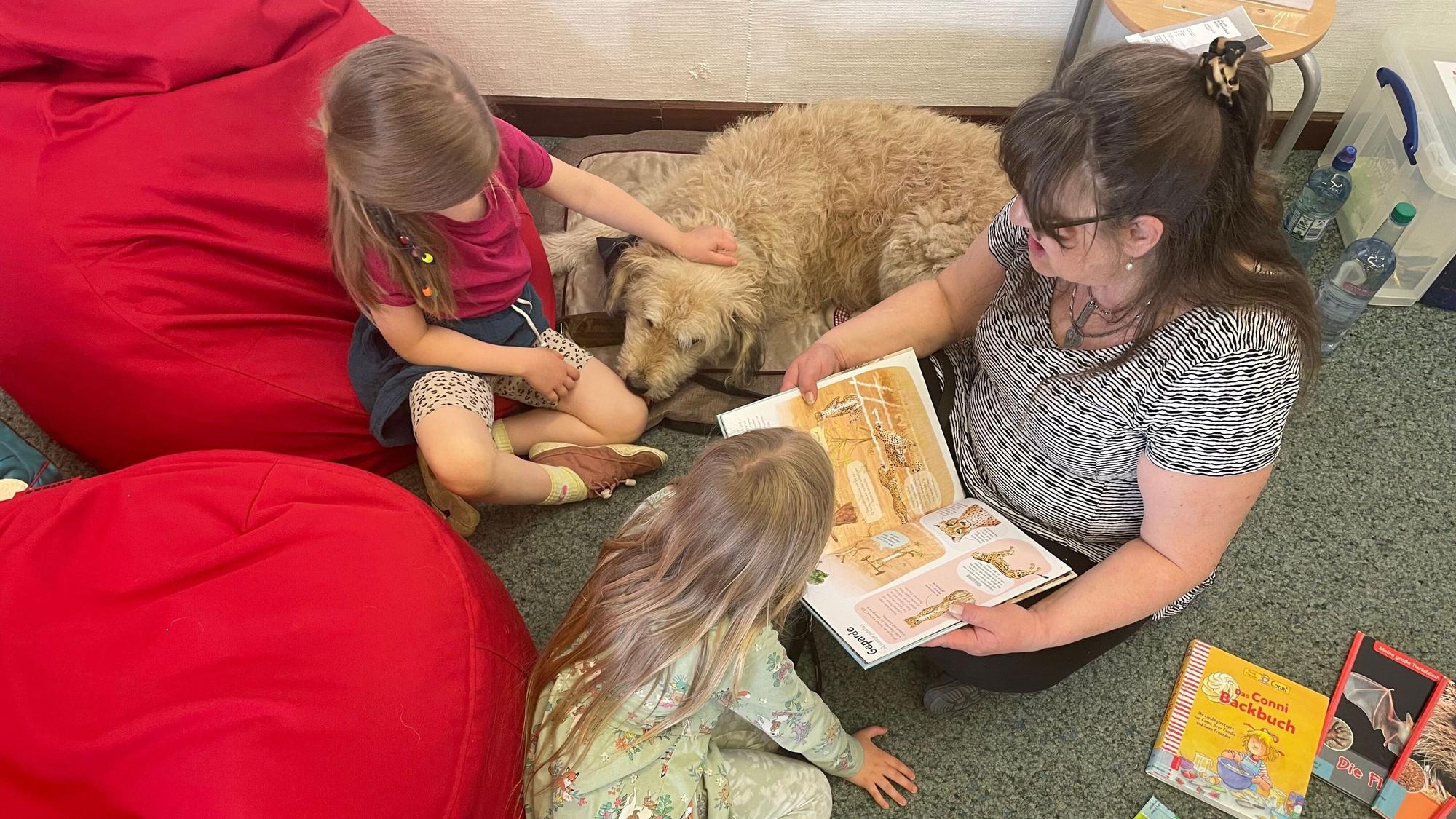 Eine Frau sitzt mit zwei Kindern und einem Hund auf dem Boden.