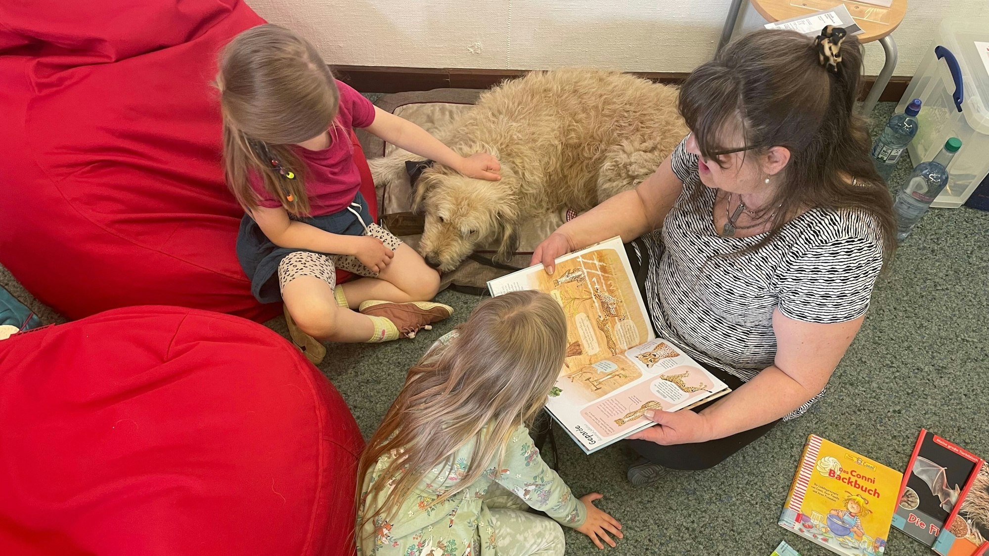 Eine Frau sitzt mit zwei Kindern und einem Hund auf dem Boden.