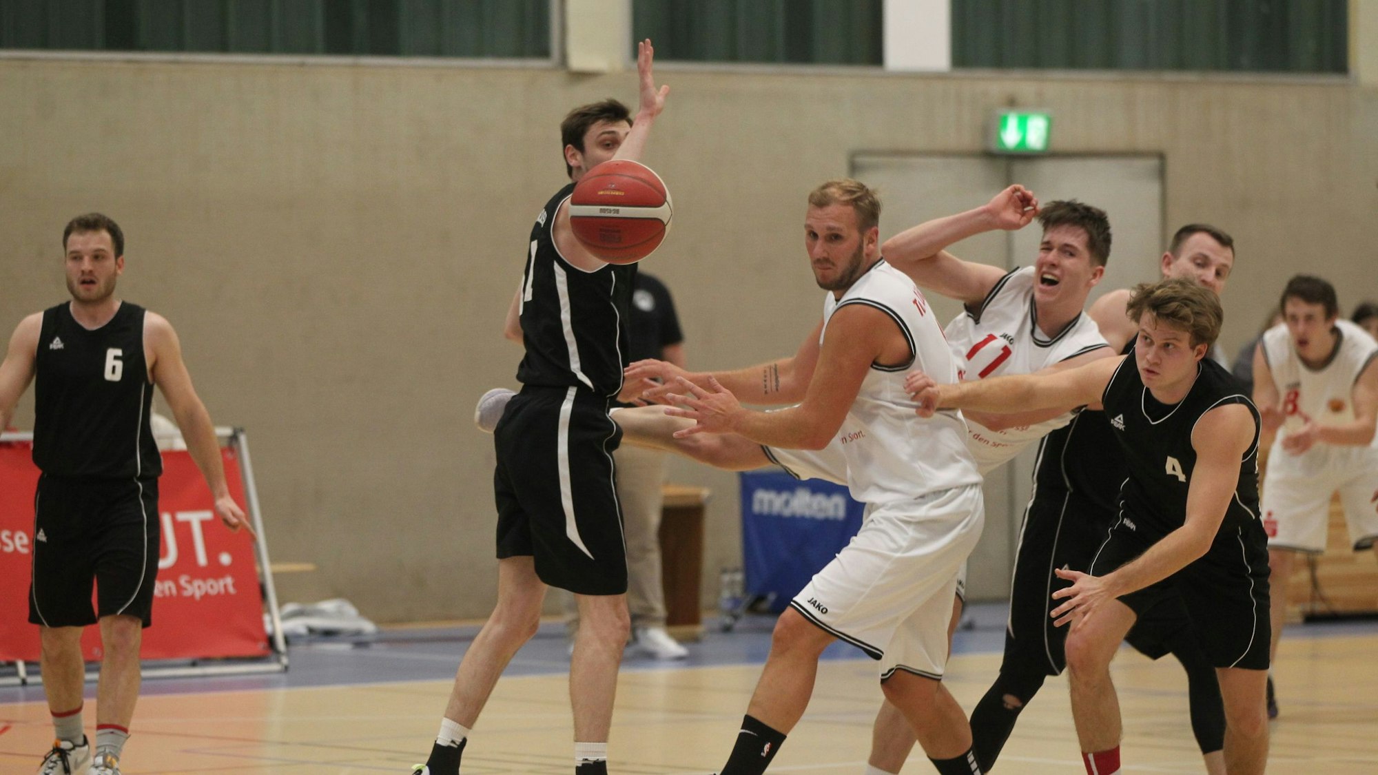 Im Basketball-Landesliga-Spiel gegen den TuS Brauweiler gerät Jan Philipp Thomas (Nr. 11) ins Straucheln. Vor ihm sein Mitspieler Christoph Gier. Der Ball ist weit weg, alle schauen ihm hinterher.