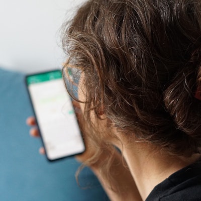 Eine junge Frau hält ihr Smartphone in der Hand und liest eine Whatsapp-Nachricht.