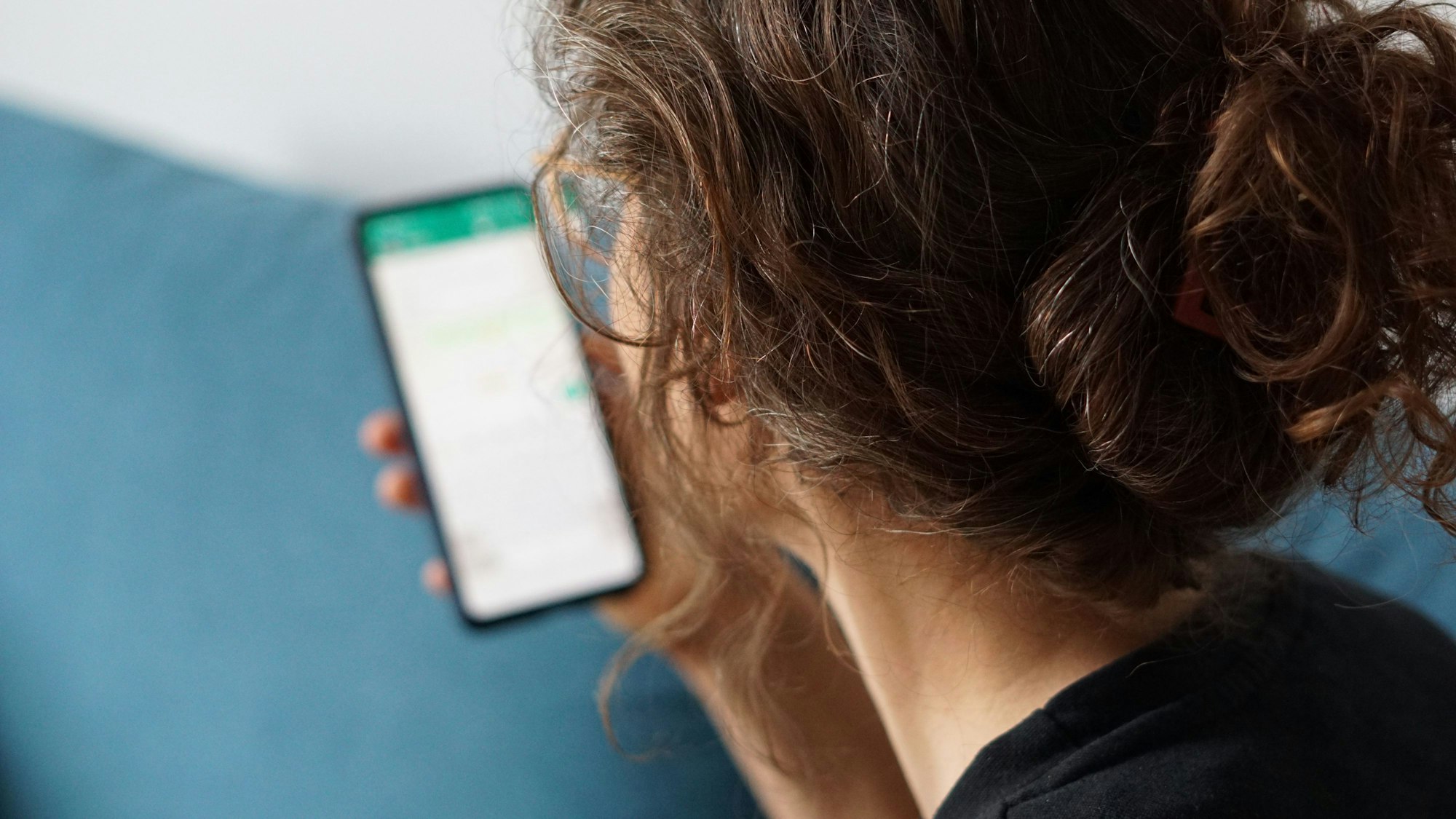 Eine junge Frau hält ihr Smartphone in der Hand und liest eine Whatsapp-Nachricht.