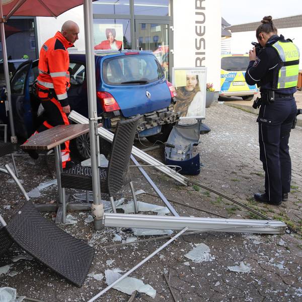Ein Polizist fotografiert einen Kleinwagen, der in den Trümmern einer Außengastronomie steht, Glasscherben und zerstörte Möbel liegen auf dem Pflaster.