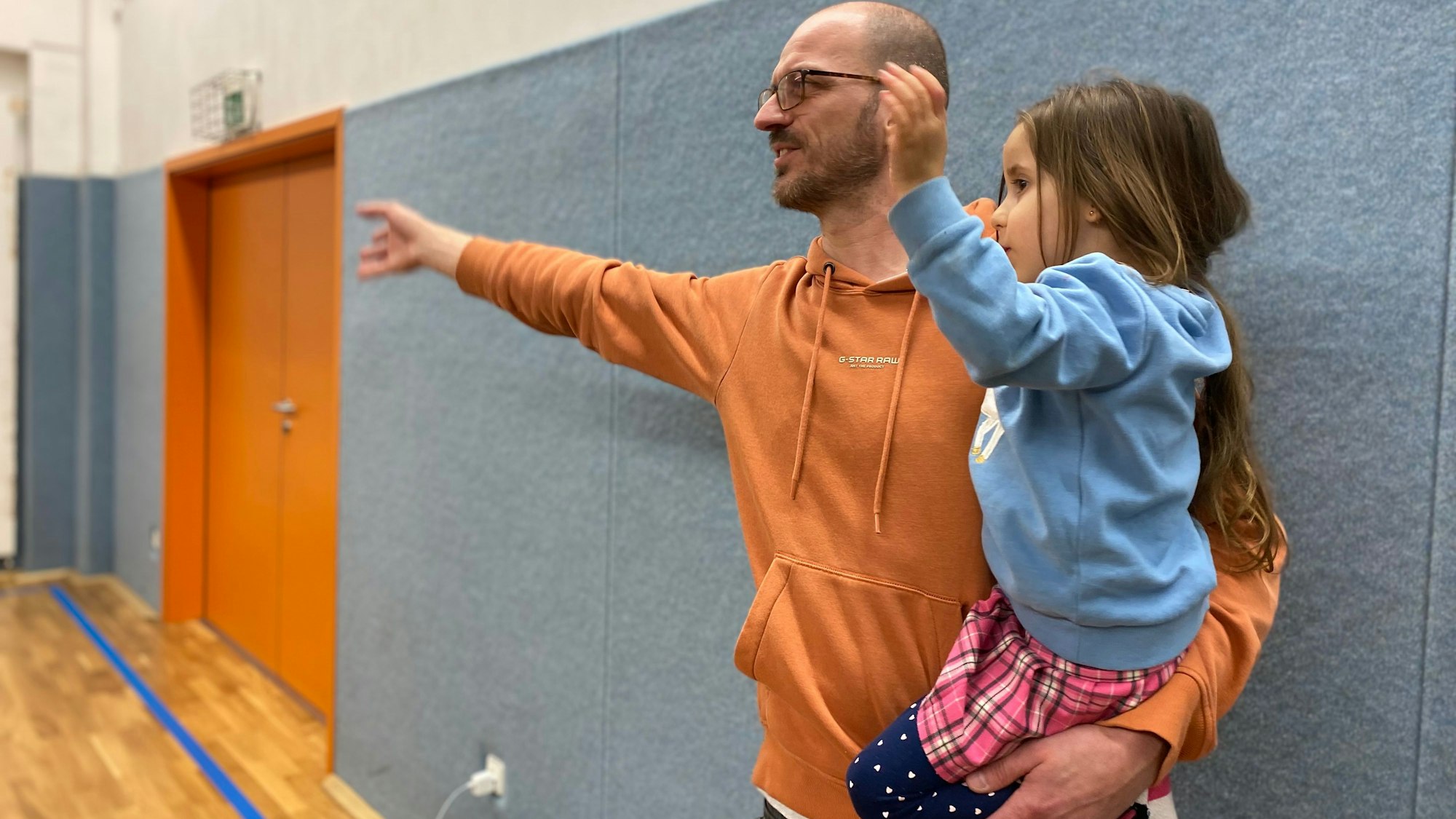Lucas Theisen hält seine Tochter auf dem Arm. Beide haben jeweils einen Arm ausgestreckt.