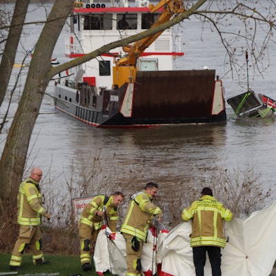 Das Bild zeigt Feuerwehrmänner am Ufer in Wesseling am Rhein.