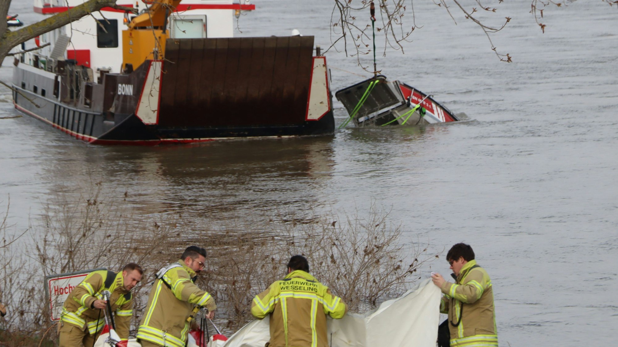 Das Bild zeigt Feuerwehrmänner am Ufer in Wesseling am Rhein.