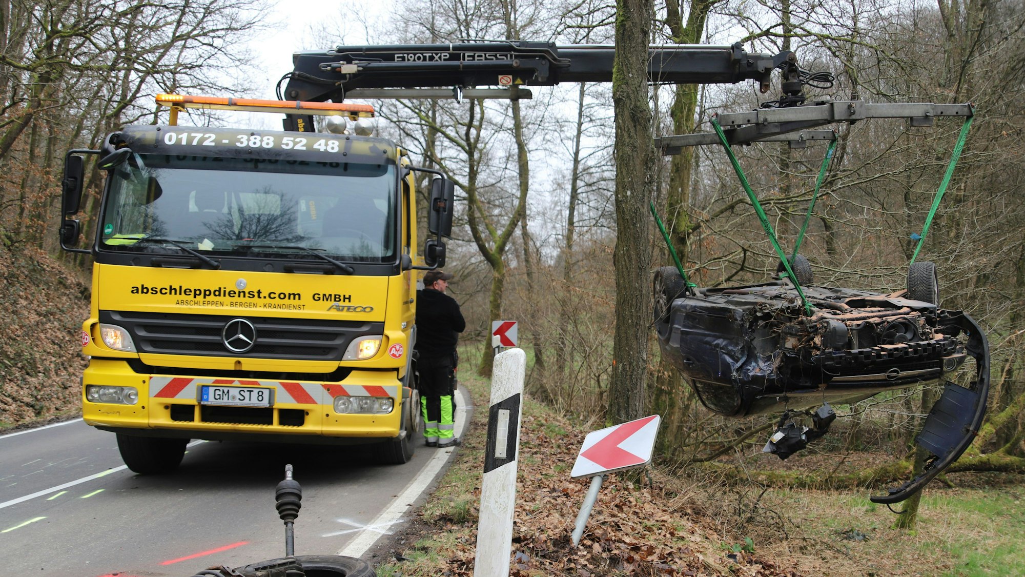 Ein Abschleppwagen hebt einen auf dem Dach liegenden Kleinwagen aus einer Wiese heraus.