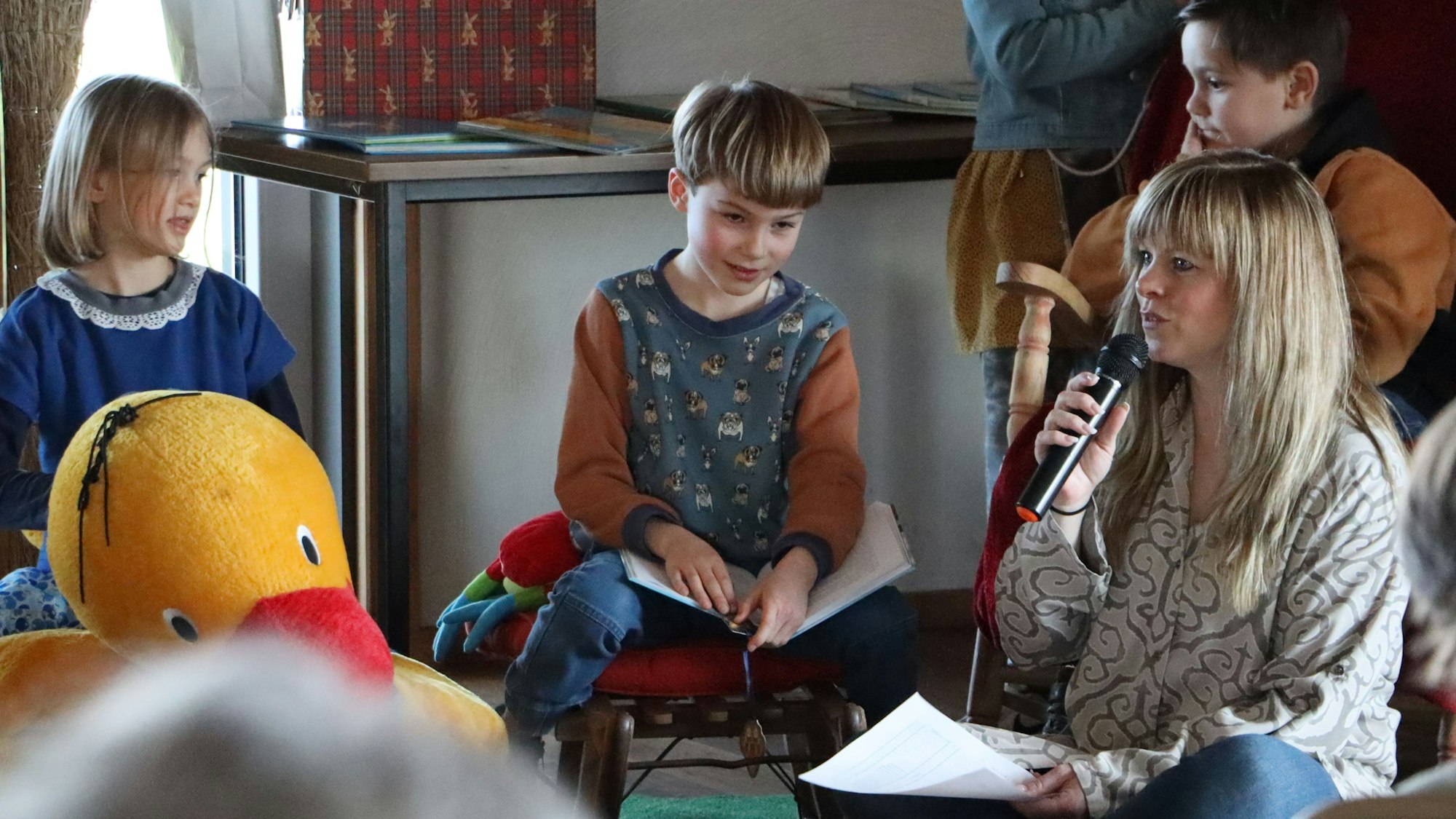 Danica Lorbach moderiert mit Mikrofon in der Hand. Zwei Kinder hören zu.