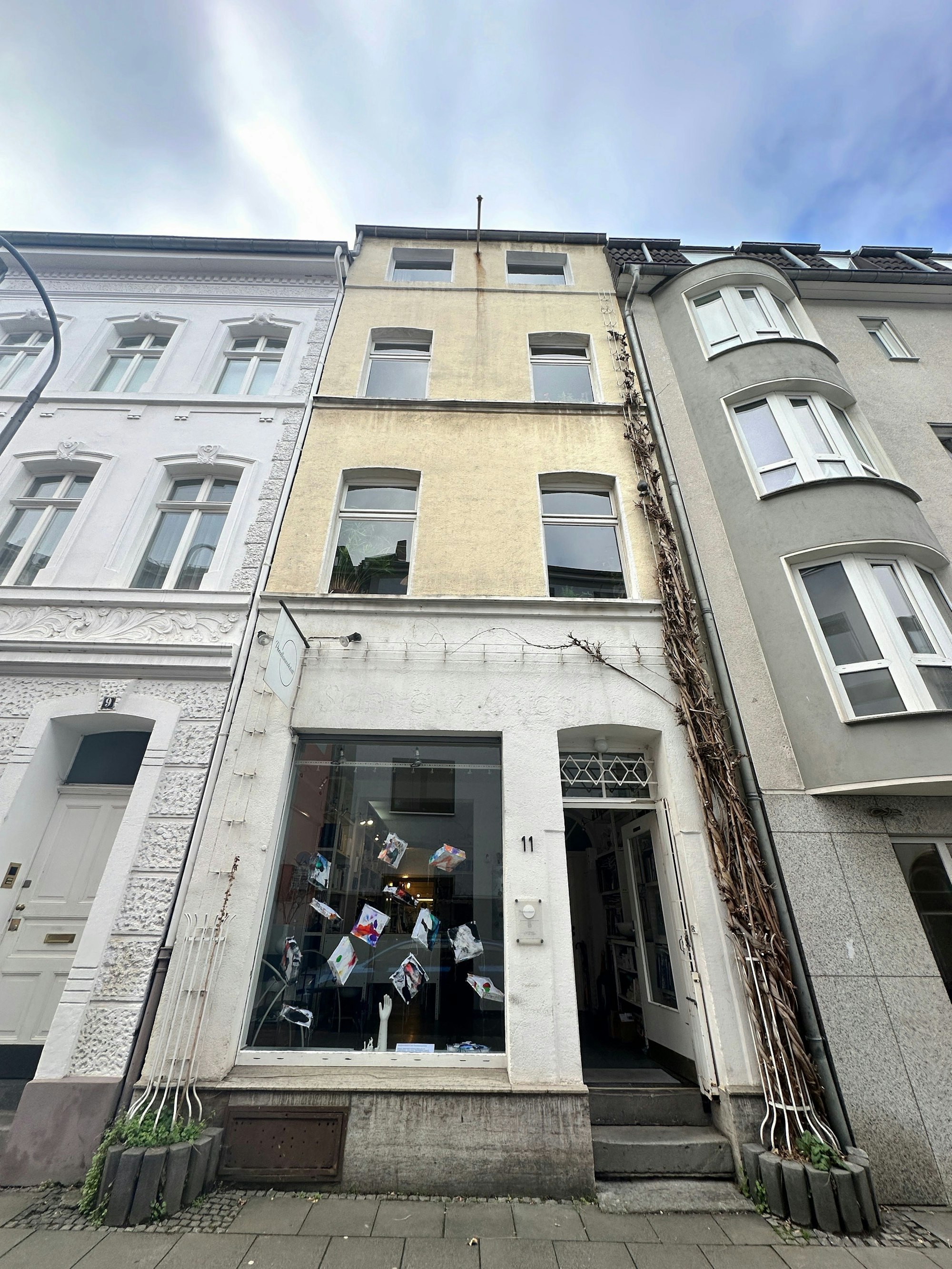 Blick auf ein schmales Haus mit zwei Fenstern pro Etage und einem Ladenlokal im Erdgeschoss