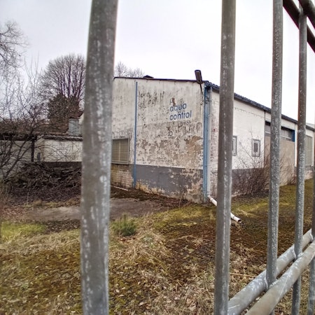 Ein heruntergekommenes Industriegebäude hinter einem Zaun mit der Aufschrift „Aqua Control“.