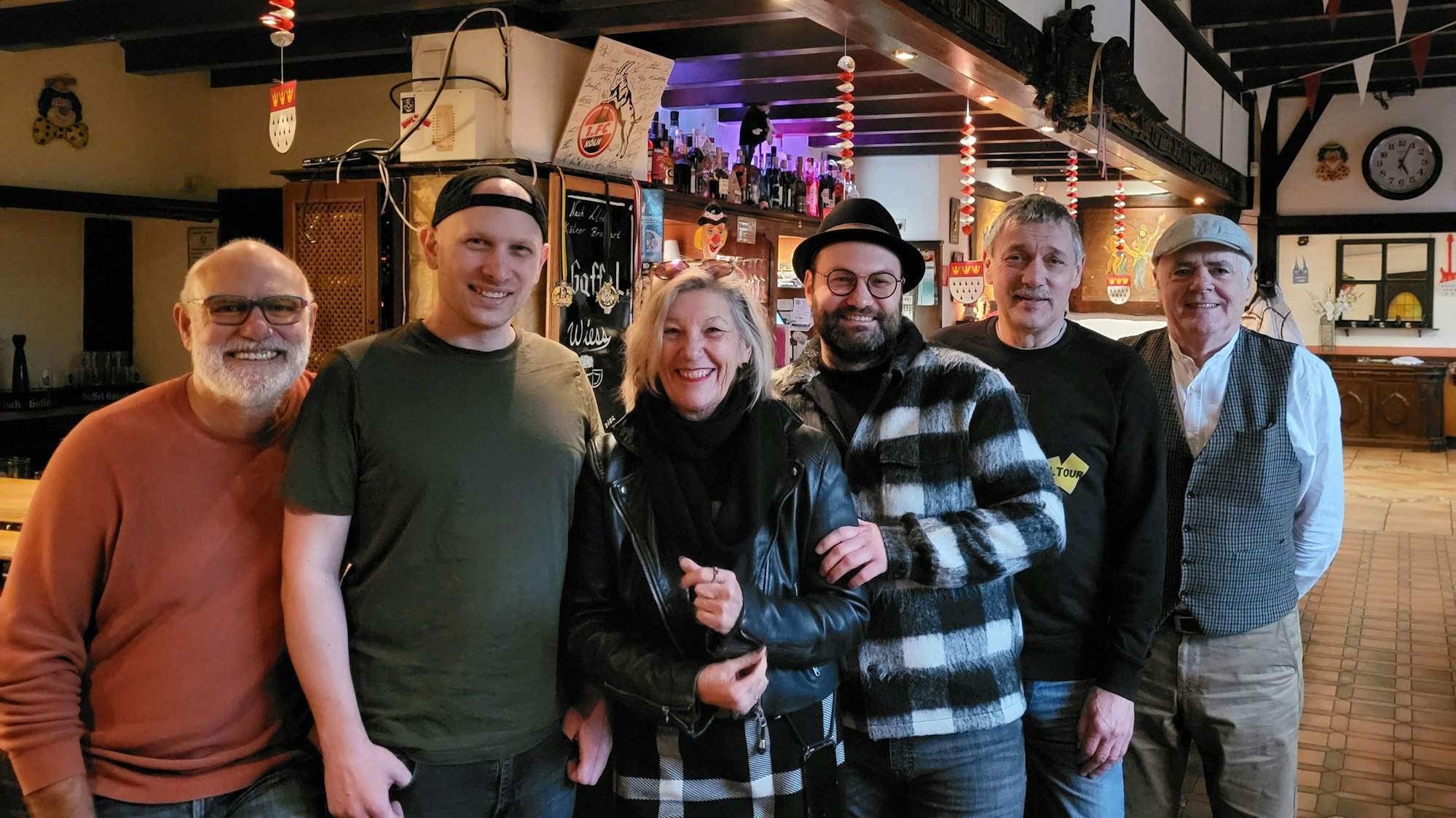 Eine Gruppe von gut gelaunten Männern und Frauen vor einer Theke im Schankraum einer Kneipe.