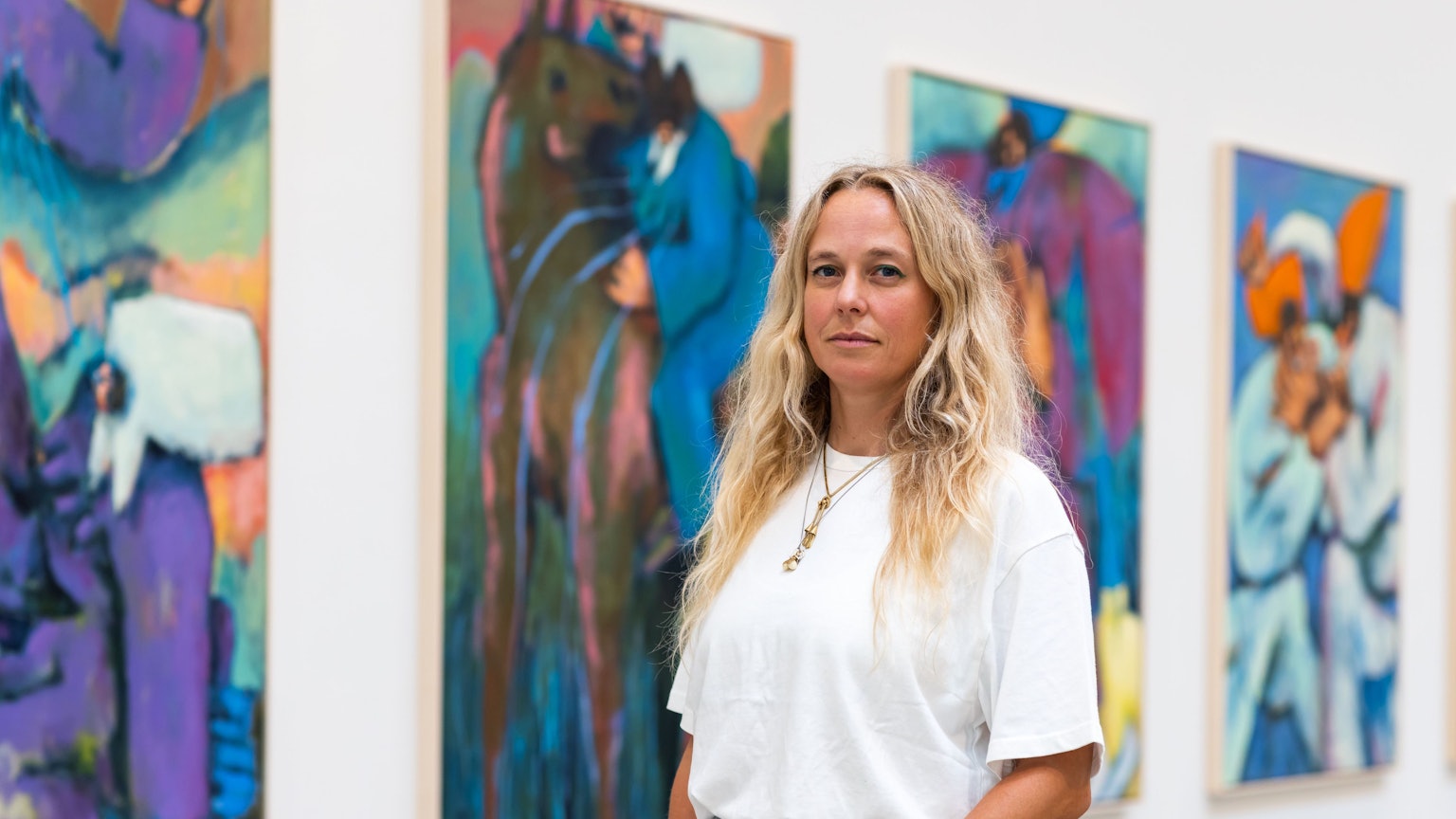 Eine Frau steht vor einer Wand mit Kunstwerken.