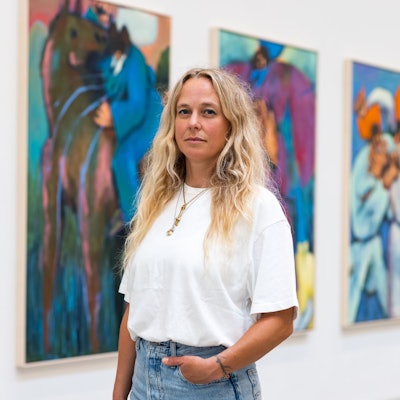 Eine Frau steht vor einer Wand mit Kunstwerken.