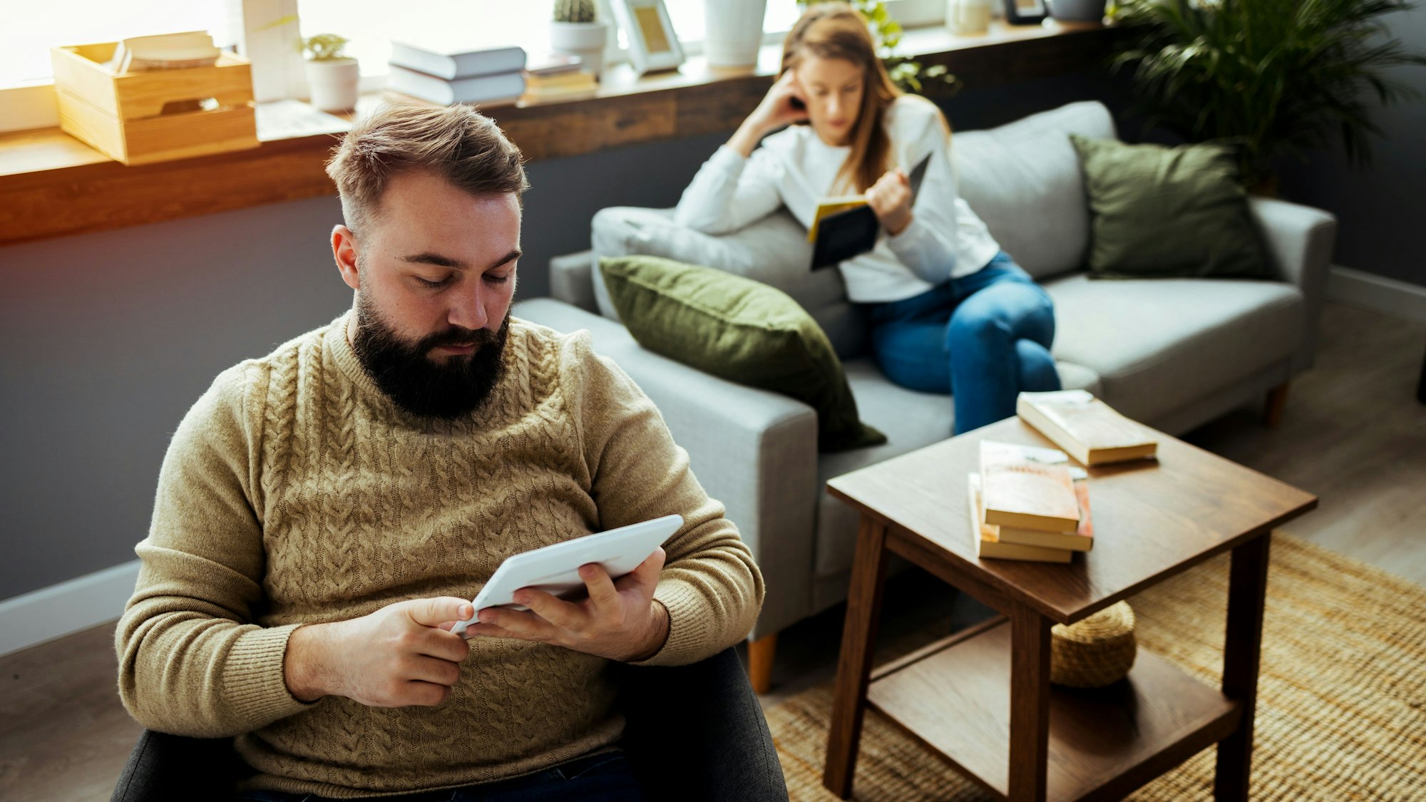 Paar sitzt im Wohnzimmer, beide lesen für sich.