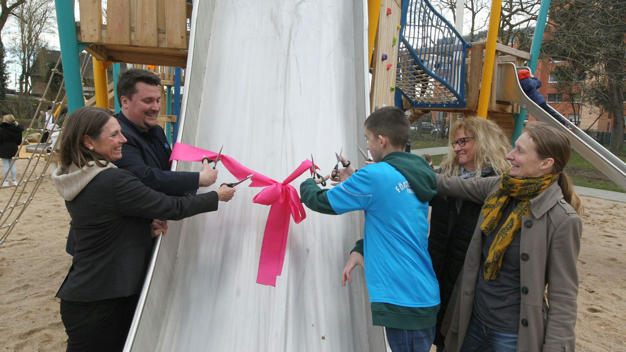 Übergabe Spielplatz Alemannenstraße in Sieglar an die Kinder (v.l.): Die Beigeordnete Tanja Gasper, Bügermeister Alexander Biber, Jason (11), Irene Selmani und Projektleiterin Suzanne Schwirian durchschneiden die rosa Schleife.