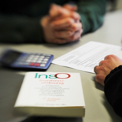 Ein Mann sitzt in einem Beratungsgespräch bei der Schuldner- und Insolvenzberatungsstelle. Ein Mitarbeiter füllt das Formular aus, im Vordergrund liegt ein Buch über die Insolvenzordnung.