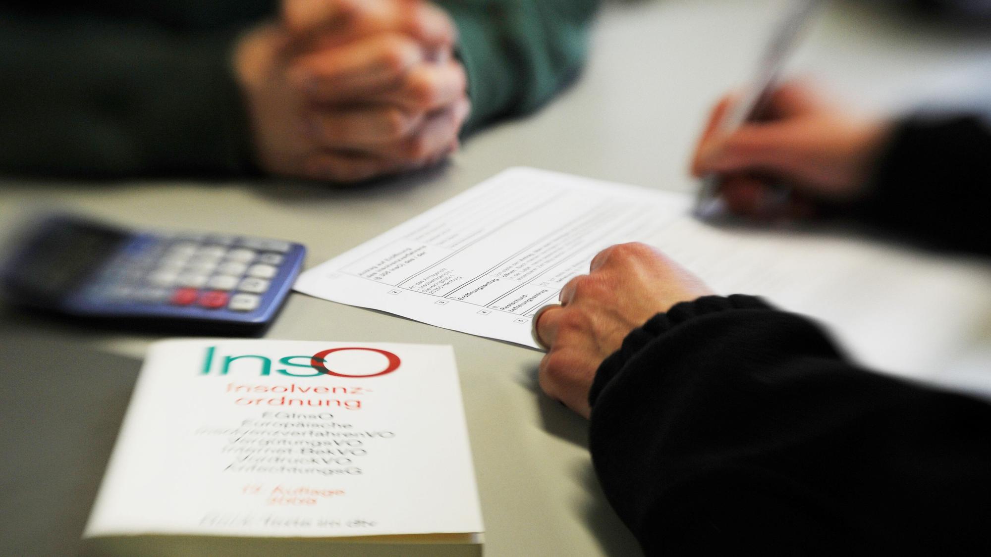 Ein Mann sitzt in einem Beratungsgespräch bei der Schuldner- und Insolvenzberatungsstelle. Ein Mitarbeiter füllt das Formular aus, im Vordergrund liegt ein Buch über die Insolvenzordnung.