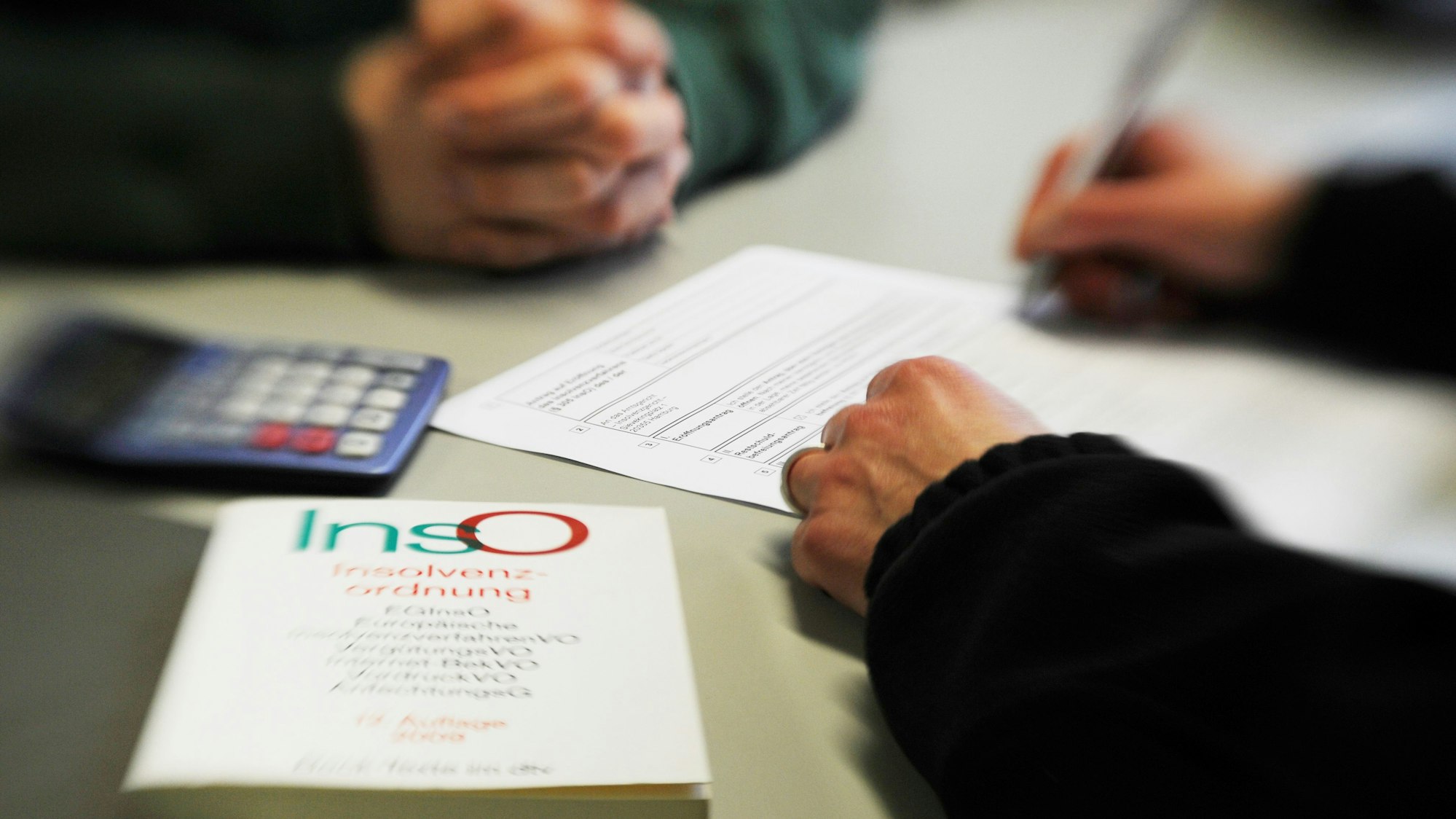 Ein Mann sitzt in einem Beratungsgespräch bei der Schuldner- und Insolvenzberatungsstelle. Ein Mitarbeiter füllt das Formular aus, im Vordergrund liegt ein Buch über die Insolvenzordnung.