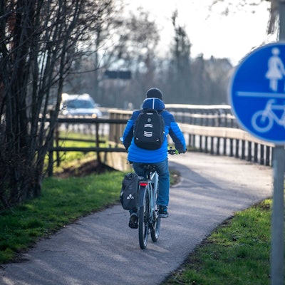 Ein Radfahrer, der an einem Radwegschild vorbeifährt, ist von hinten zu sehen.