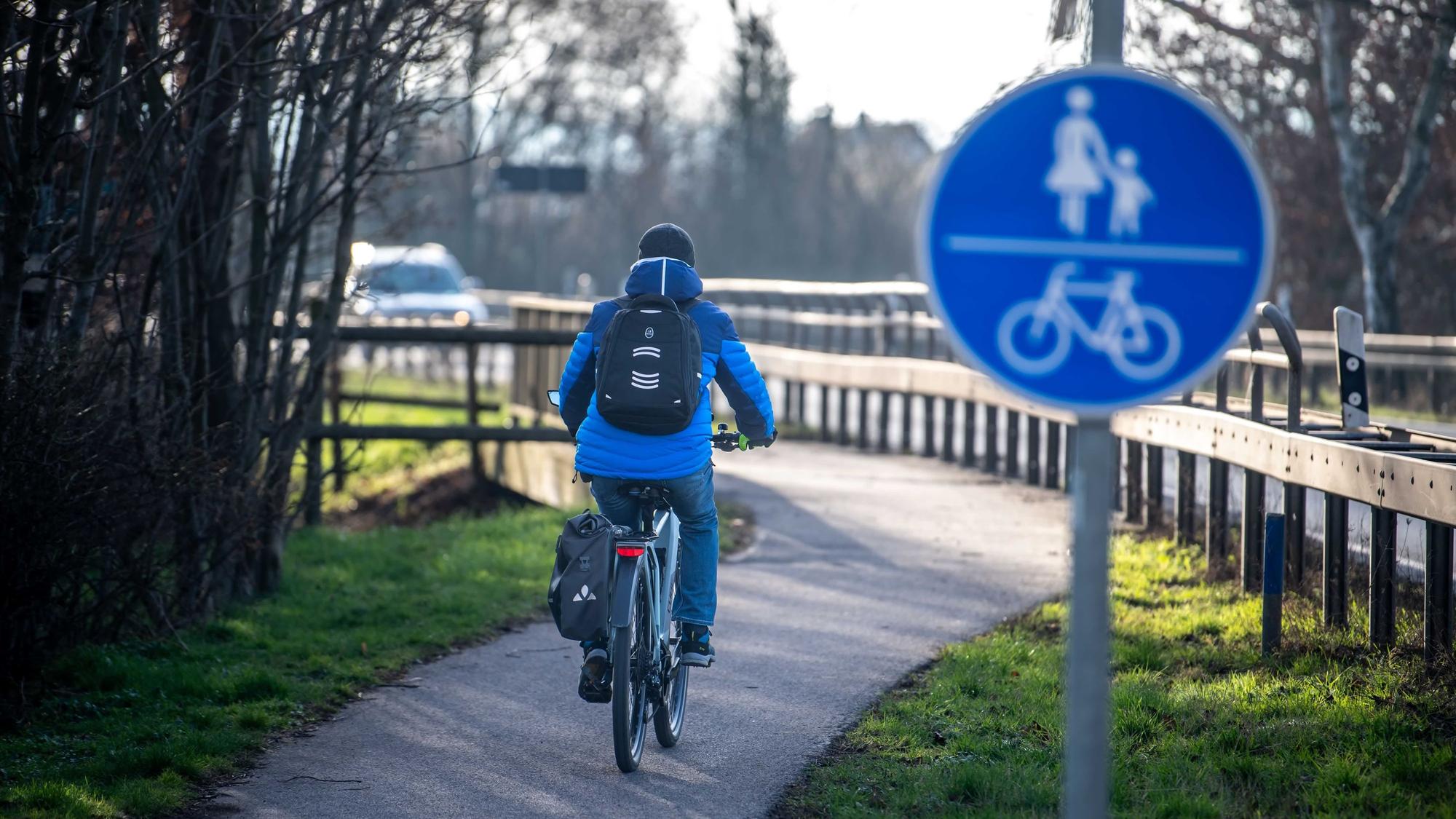 Ein Radfahrer, der an einem Radwegschild vorbeifährt, ist von hinten zu sehen.