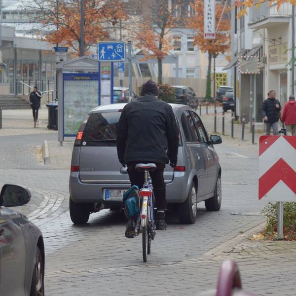 Das Bild zeigt einen Radfahrer in der Euskirchener Innenstadt. Vor und hinter ihm fahren Autos.