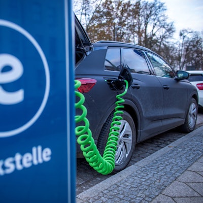 Das Symbolbild zeigt ein Elektrofahrzeug, das an einer blauen Ladesäule mit der Aufschrift „Tankstelle“ steht.