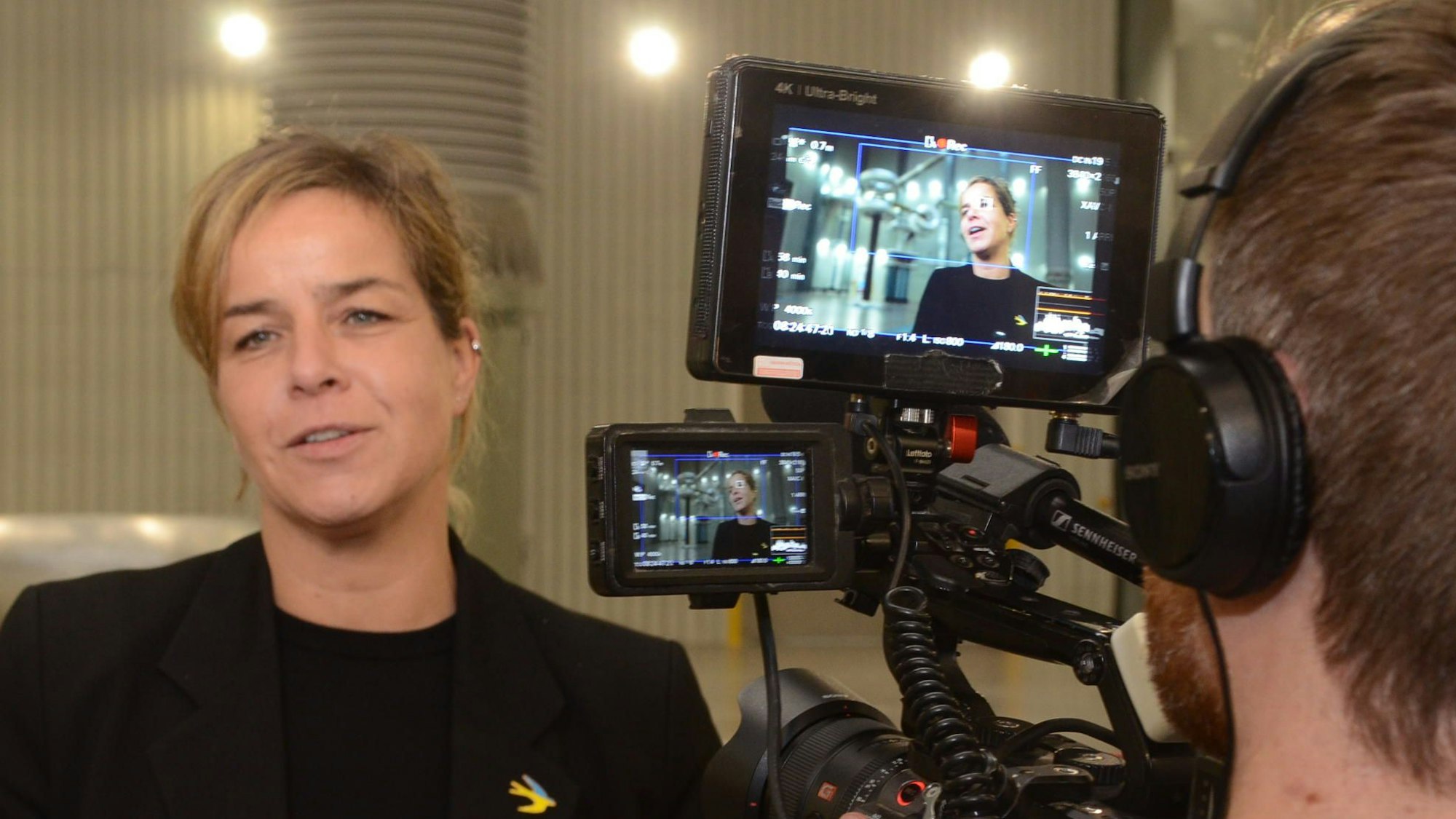 Eine Frau spricht vor einer Kamera. Sie ist auf gleich zwei Bildschirmen zu sehen.