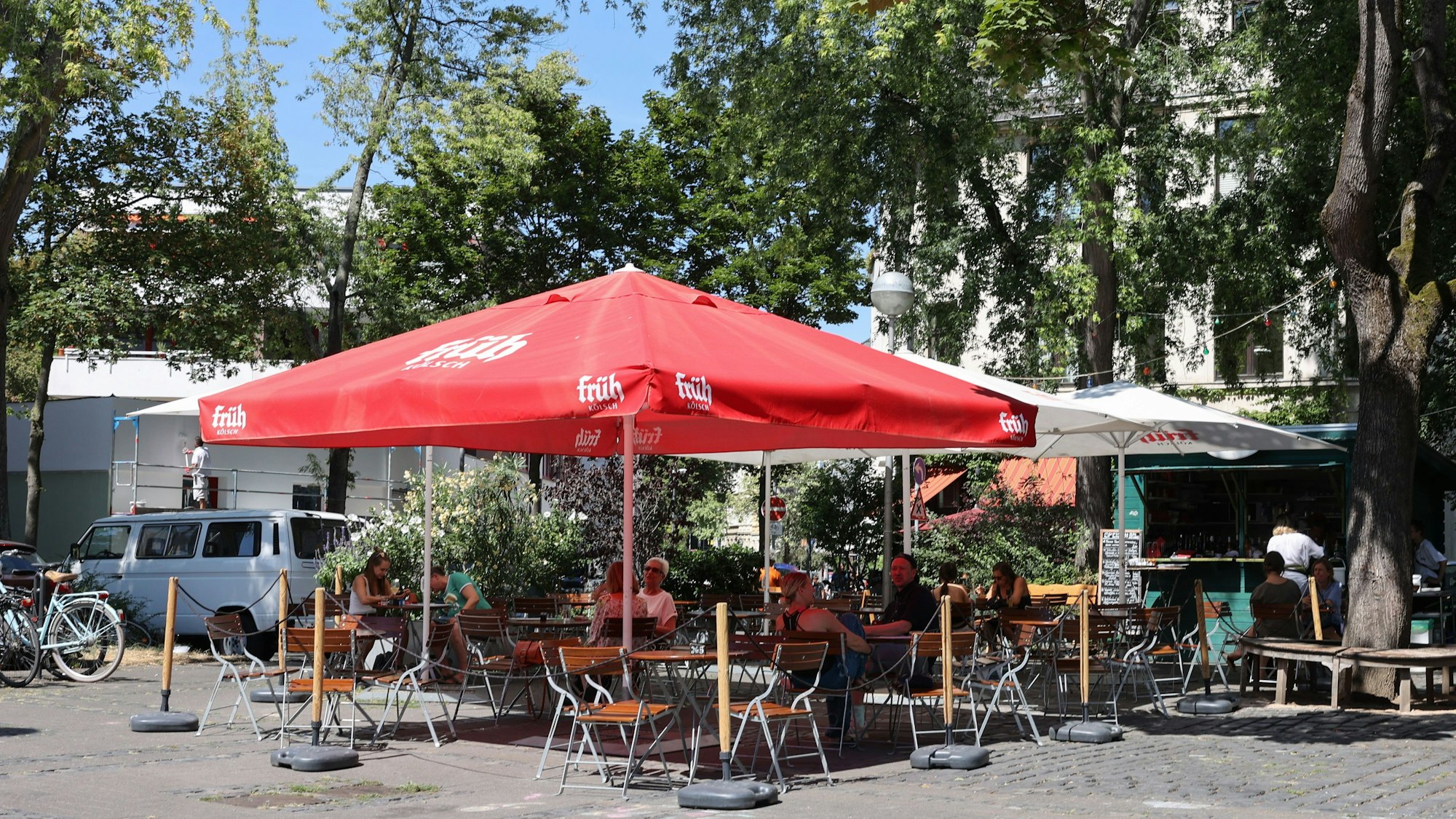 Stühle und Tische stehen auf einem Platz unter einem Sonnenschirm.