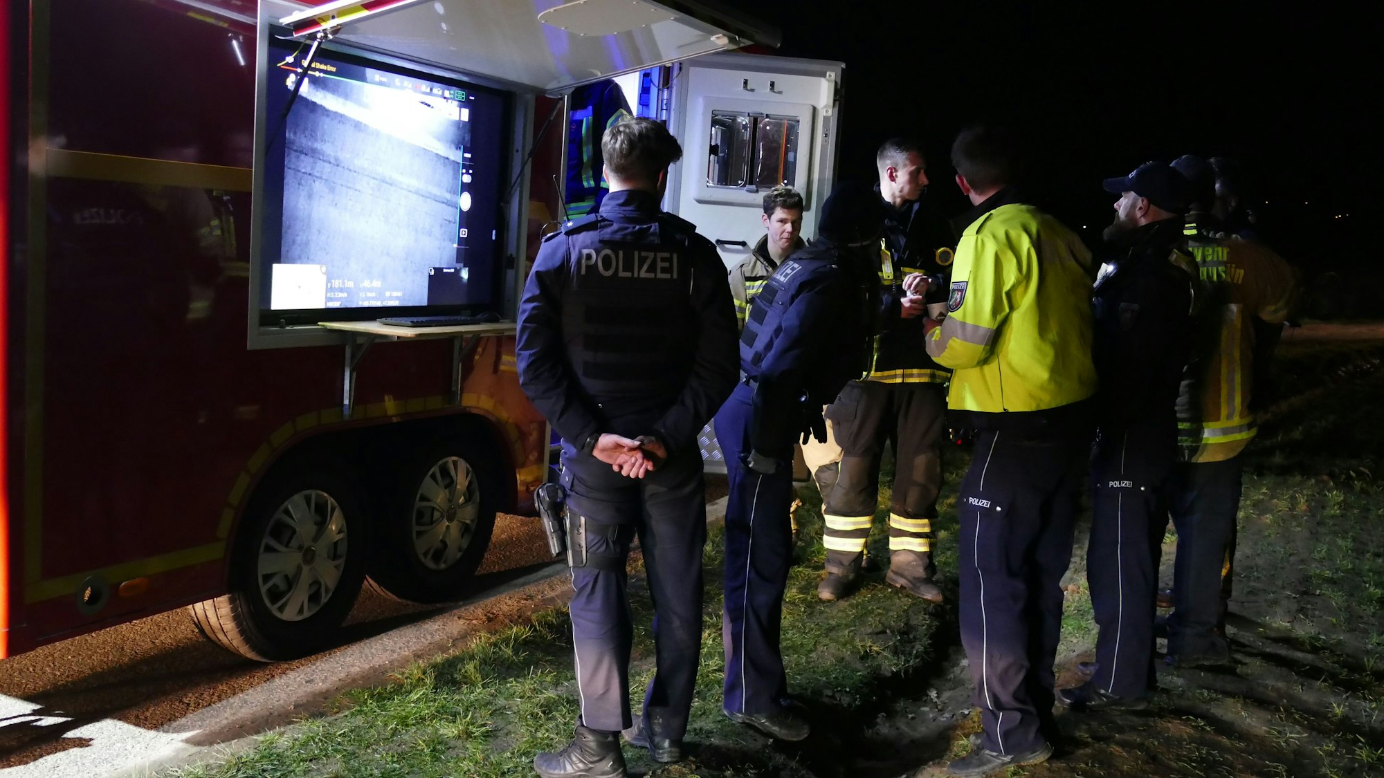 Polizisten und Feuerwehrleute stehen vor einem Feuerwehr-Fahrzeug mit Bildschirm.