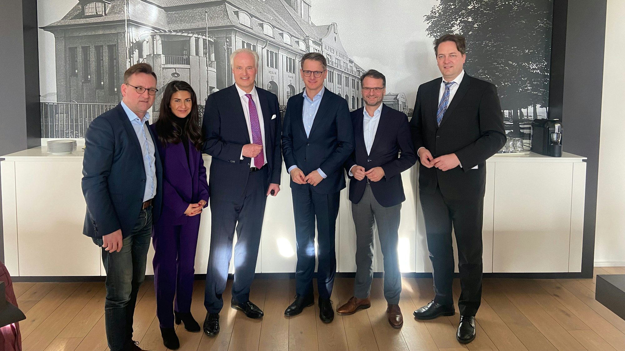 Fünf Männer und eine Frau stehen vor einem historischen schwarz-weiß-Bild eines Firmengebäudes.