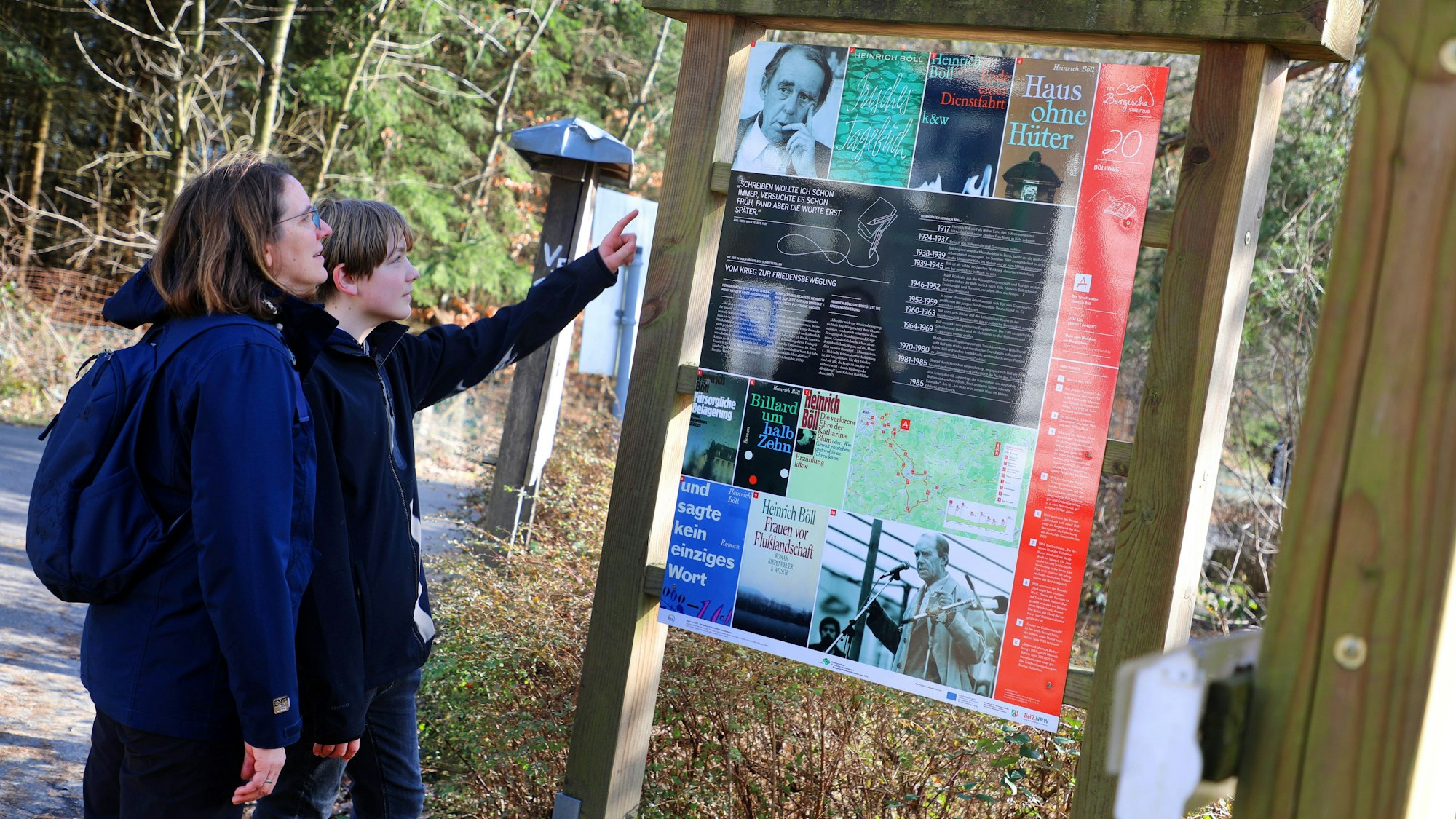 Eine Frau und ein Kind stehen an der Starttafel des Böllwegs bei Much und lesen.