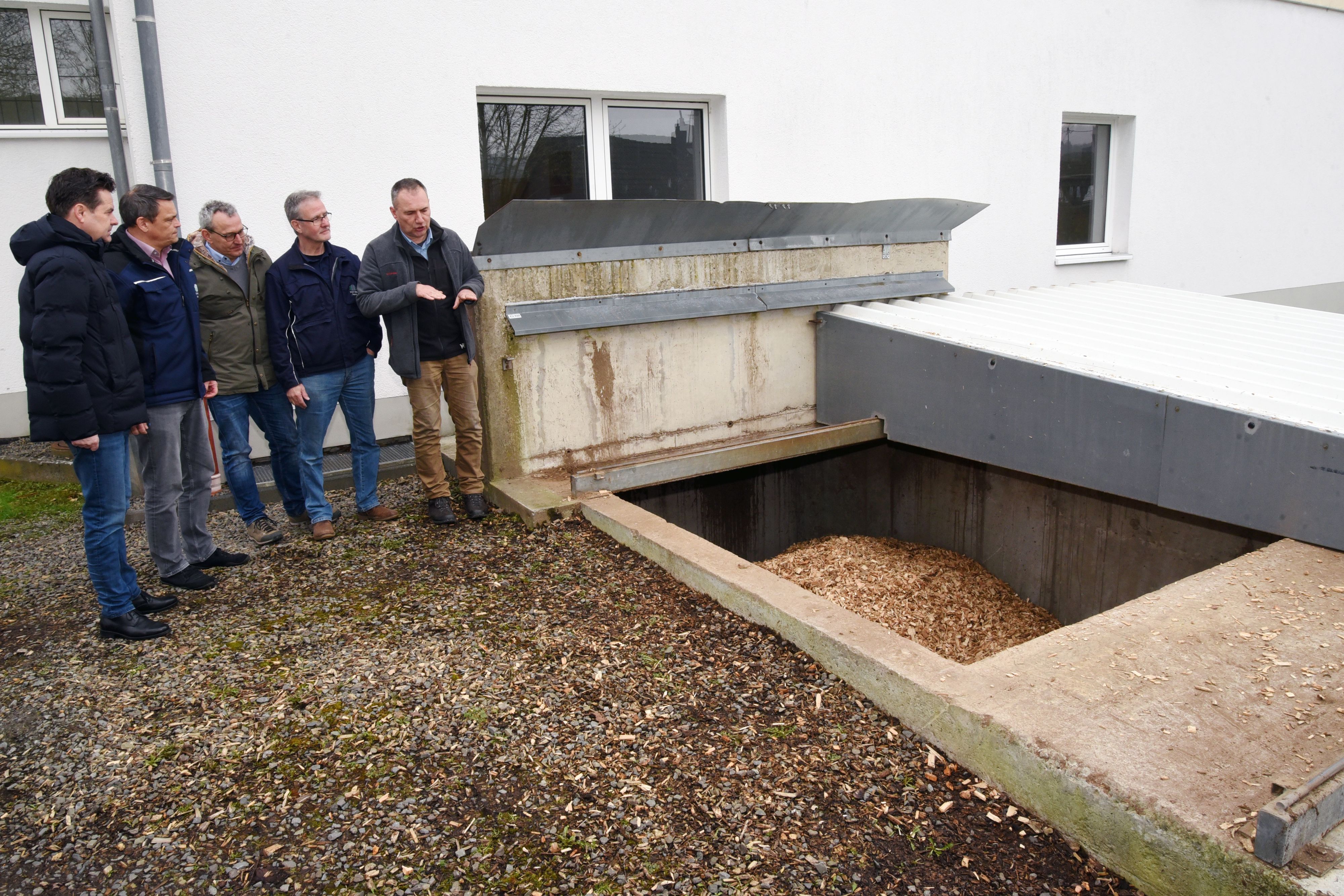 Fünf Männer stehen vor dem offenen Bunker einer Holzhackschnitzelheizung.