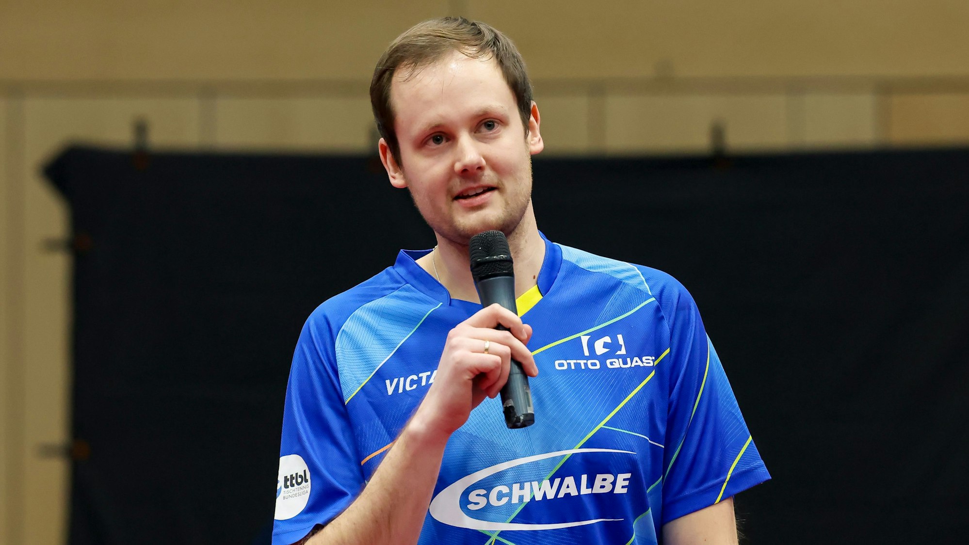 Bergneustadts Trainer Frederik Duda hat ein Mikrophon in der Hand und spricht über das Spiel.