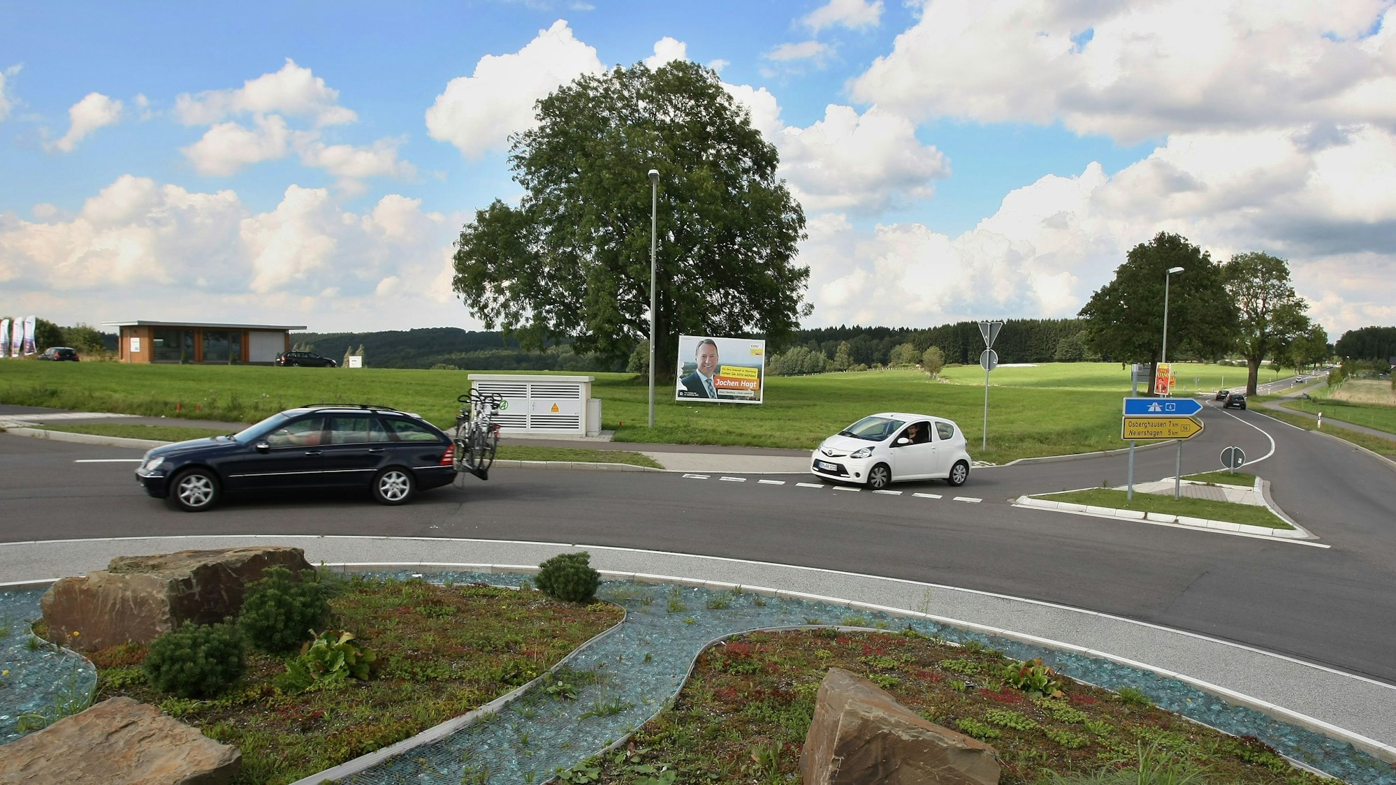 Ein Kreisverkehr und Autos im Vordergrund, dahinter eine große Wiese.