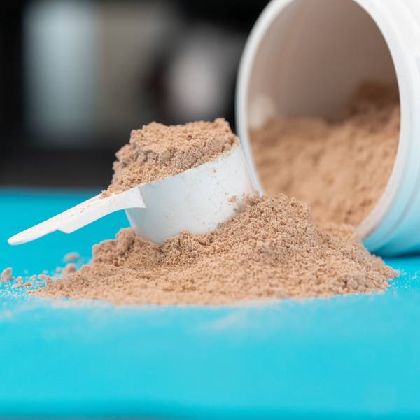 Ein Haufen Proteinpulver und ein Portionierlöffel liegen auf einer türkisen Oberfläche.