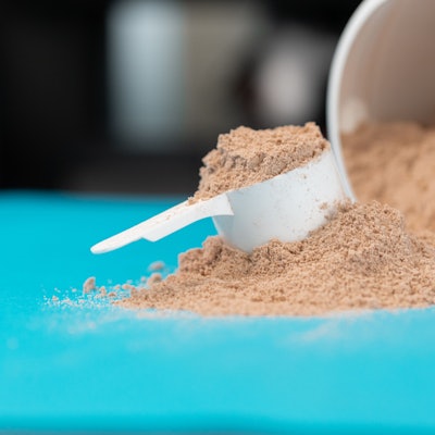 Ein Haufen Proteinpulver und ein Portionierlöffel liegen auf einer türkisen Oberfläche.