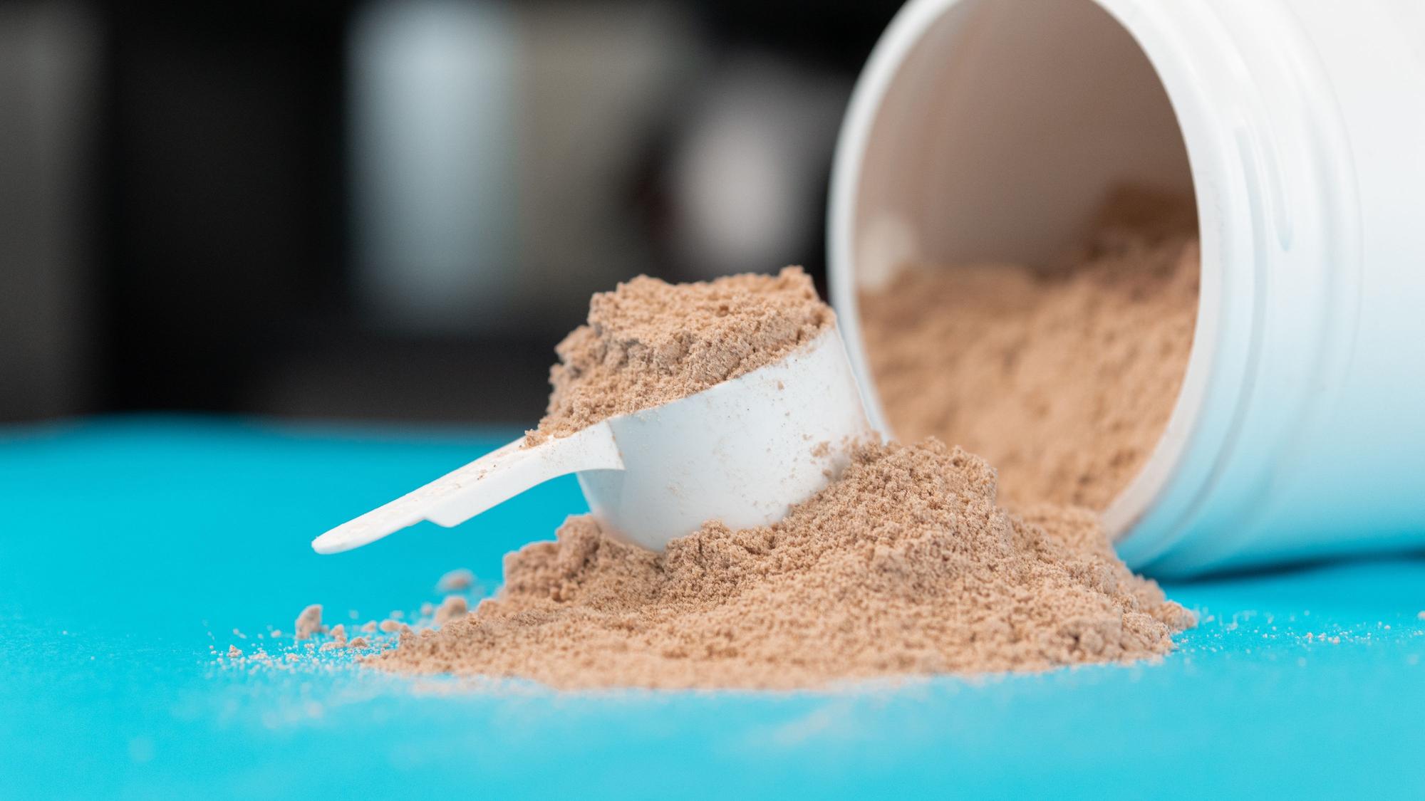 Ein Haufen Proteinpulver und ein Portionierlöffel liegen auf einer türkisen Oberfläche.