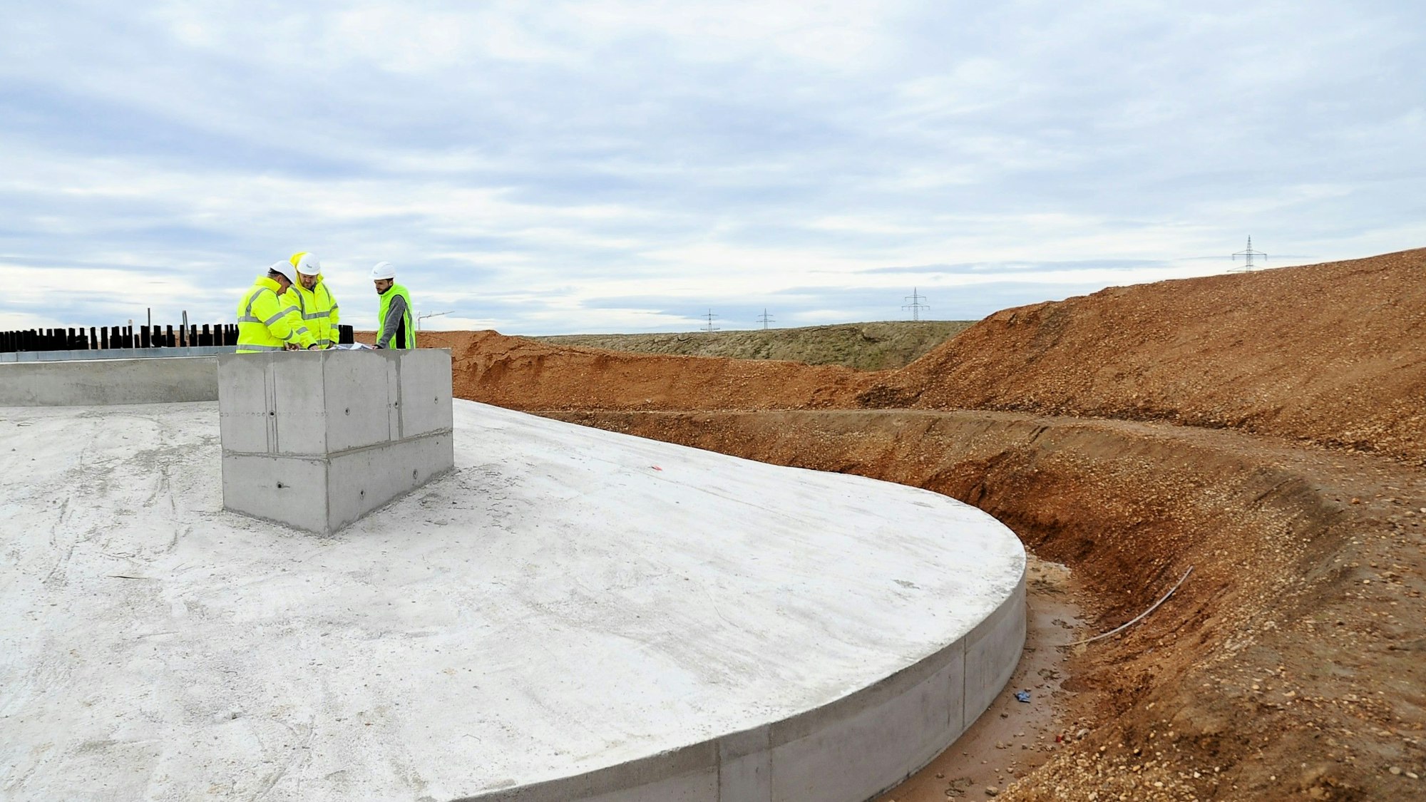 Drei Männer in Schutzkleidung stehen auf einem riesigen Fundament.