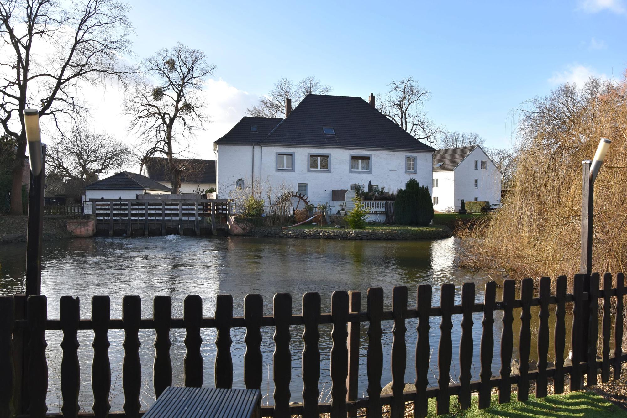 Eine weiße Wassermühle an einem Mühlteich.