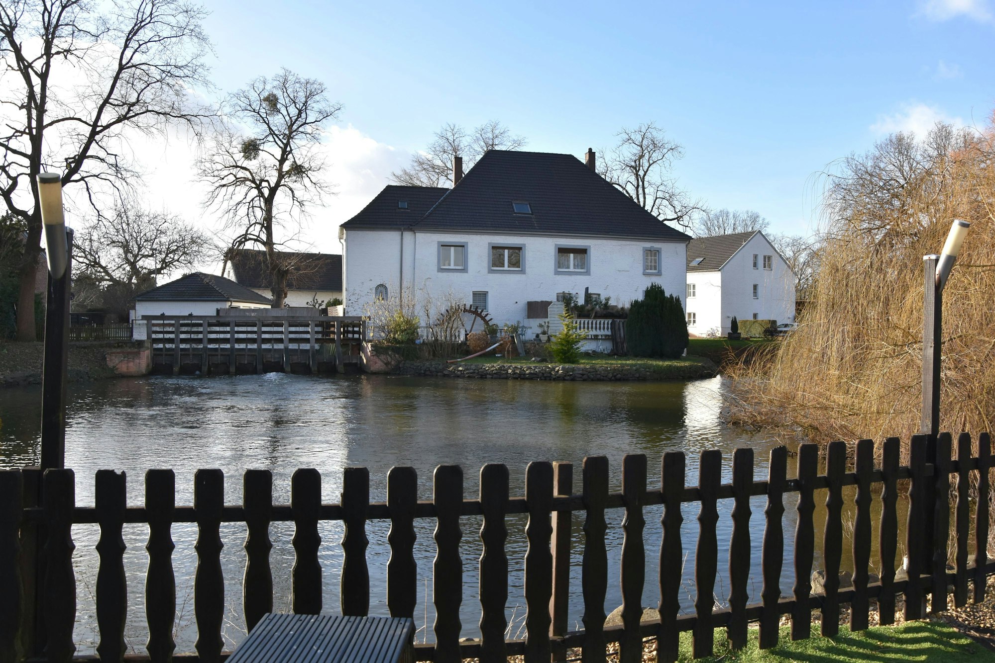 Eine weiße Wassermühle an einem Mühlteich.