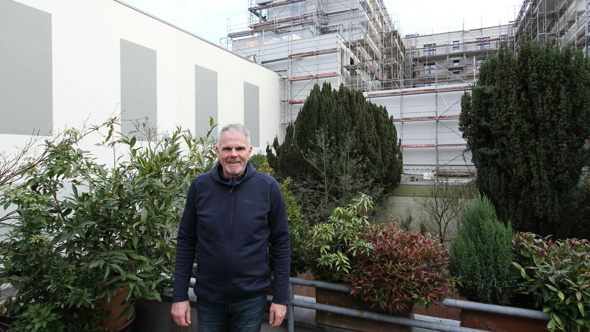 Ein Mann auf einem bepflanzten Balkon vor einem großen Wohngebäude