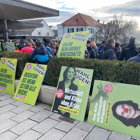 „Für jeden Missstand muss es eine einfache Ursache geben“: Aufgebrachte Landwirte protestieren mit verfremdeten Wahlplakaten beim politischen Aschermittwoch der Grünen in Biberach. Kurz darauf eskaliert die Lage vor der Halle, die Veranstaltung wird abgesagt.