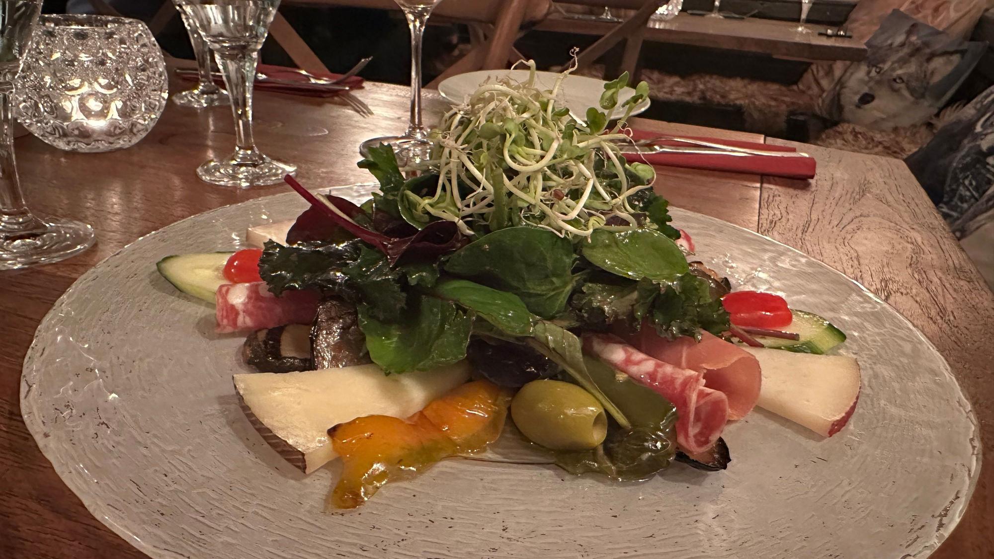 Ein Antipasti-Vorspeisenteller mit Käse, Schinken, Salat, Tomaten und Gurken.