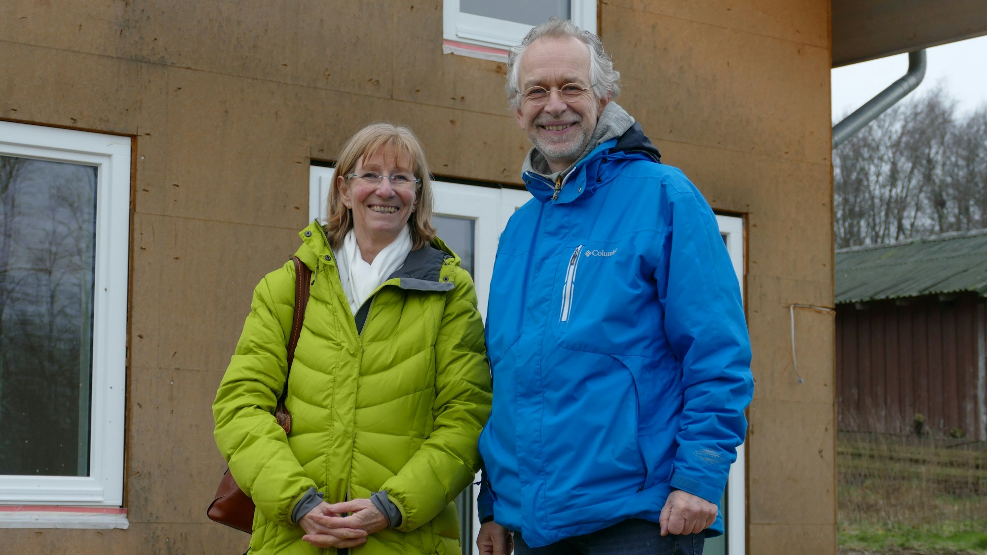 Eine Frau und ein Mann vor einem Neubau. Beide lachen.