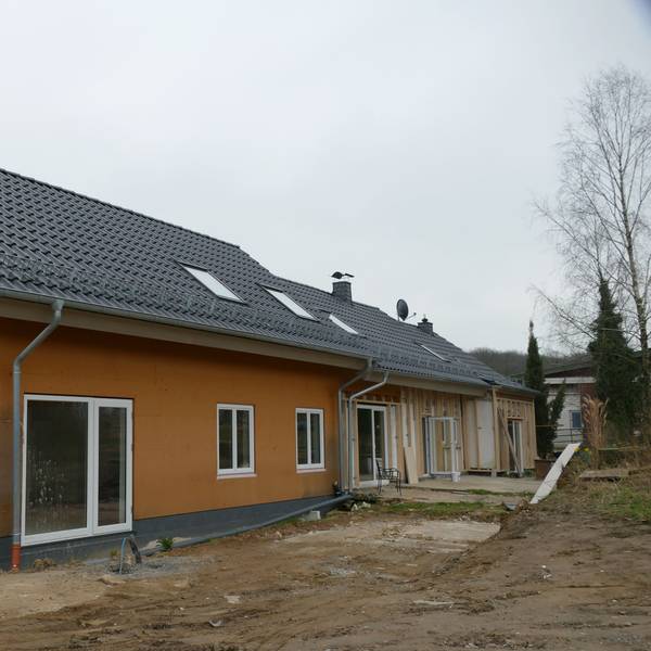 Ein Einfamilienhaus auf einem Baugrundstück. Das vordere Haus ist fertig, an zwei weiteren im Hintergrund wird noch gebaut.