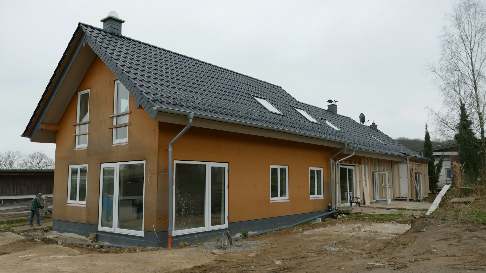 Ein Einfamilienhaus auf einem Baugrundstück. Das vordere Haus ist fertig, an zwei weiteren im Hintergrund wird noch gebaut.