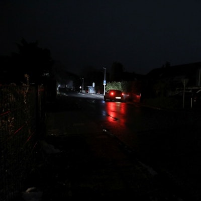 Die roten Rücklichter eines fahrenden Autos auf einer sehr dunklen Straße.