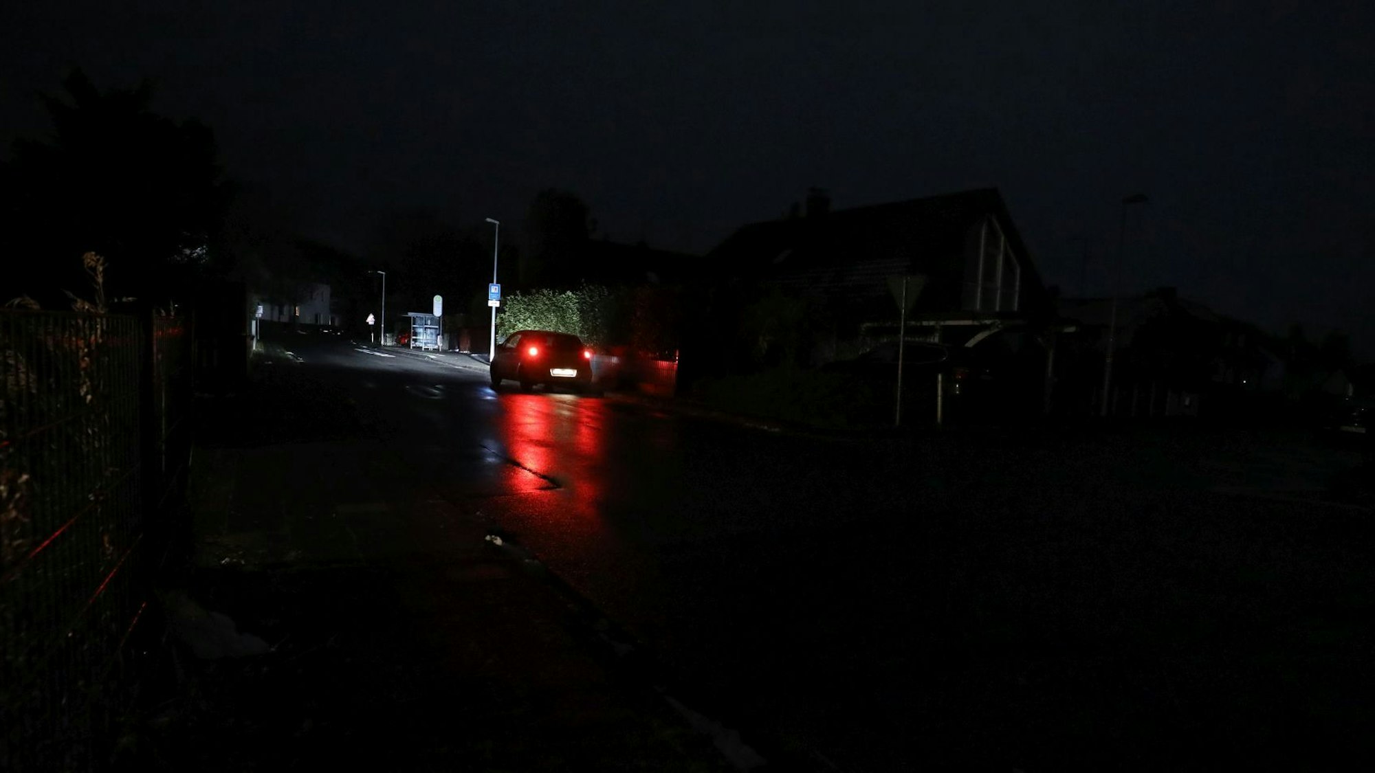 Die roten Rücklichter eines fahrenden Autos auf einer sehr dunklen Straße.